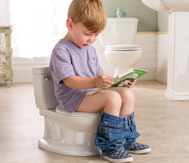 A little boy sits on potty and reads a book
