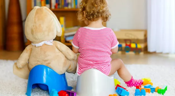 Closeup of cute little 12 months old toddler baby girl child sitting on potty. Kid playing with big plush soft toy. Toilet training concept.